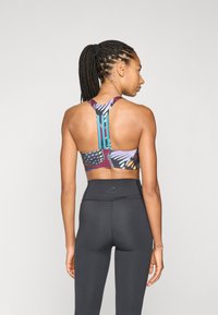 Sujetador deportivo con un patrón de mariposas multicolores; diseño de espalda cruzada; pantalones negros de cintura alta; textura suave con tirantes en contraste.