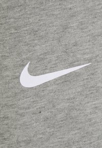 Šedá bavlněná látka má hladkou texturu a ve středu oděvu se nachází výrazné bílé logo Nike swoosh.