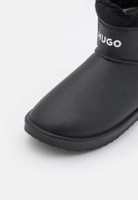 Czarne wodoodporne zimowe buty z futrzanym podszyciem i naszywką z logo "HUGO" na górnej przedniej części.