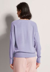 Lila gestrickter Pullover mit langen Ärmeln und gerippten Bündchen. Hat eine weiche Textur und einen lockeren Schnitt, von hinten gezeigt, kombiniert mit rosa Hosen.