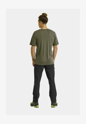 Dunkelgrünes T-Shirt mit kurzen Ärmeln und glatter Textur, kombiniert mit schwarzen Hosen im Slim-Fit-Stil und Akzenten am Unterschenkel.