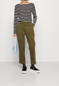 Maglietta a righe bianche e nere a maniche lunghe, pantaloni verde oliva, scarpe slip-on nere con suole bianche e una piccola borsa a tracolla blu chiaro.