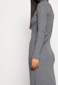 Robe en tricot gris à côtes avec col montant et manches longues, présentant une silhouette ajustée et une texture douce.