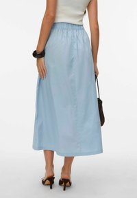 Lyseblå midinederdel med elastiklinning, glat tekstur og enkelt design. Bruges med sorte sandaler med hæl og en lille taske.