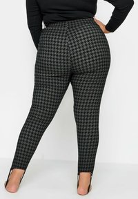 Leggings de patrón de espiga negra con una cinturilla alta y un ajuste entallado. Presentan aberturas laterales en los tobillos para añadir detalle y estilo.
