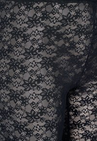 Zwarte kanten legging met een bloemenpatroon en verfijnde details. De textuur is doorschijnend met een elastische tailleband voor een goede pasvorm.