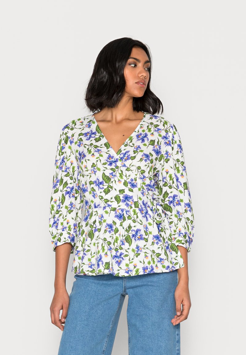 Blusa floral branca com flores azuis e folhas verdes, decote em V, mangas três quartos e design de cintura peplum. Material em algodão.