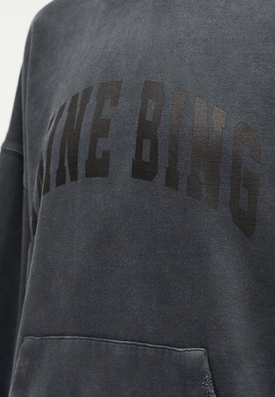 Sweat-shirt gris foncé avec de grandes lettres noires formant le texte « KING BING » sur la poitrine et une poche avant en dessous.