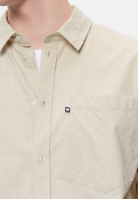 Beige gestreept overhemd met knoopsluiting, een kraag, een enkele borstzak en een klein zwart logo-patch. Zachte stof met een subtiele textuur.