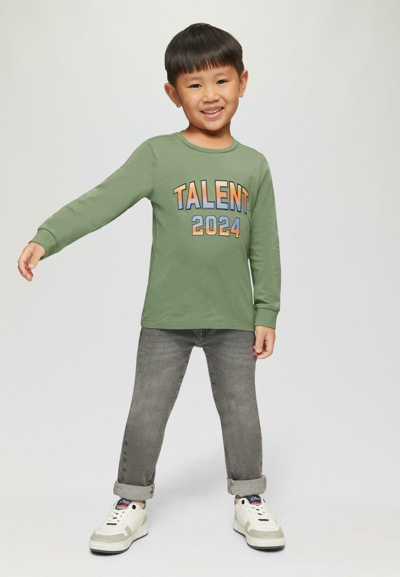 Grünes Langarmshirt mit dem Aufdruck "TALENT 2024" in mehrfarbigem Text, kombiniert mit grauen Jeans und weißen Sneakers mit grauen Akzenten.