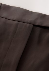 Tela marrón con una textura suave, con un borde doblado y detalles sutiles de costura. El material parece duradero y confeccionado a medida.