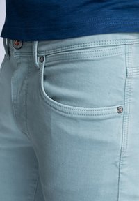 Vaqueros de algodón azul claro con una textura suave, que cuentan con cuatro bolsillos, una cremalleras y detalles de costura sutiles.