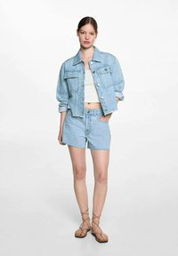 Ljusblå denimjacka med två framfickor och en kortad design, i kombination med matchande ljusblå shorts med stjärnmönster.