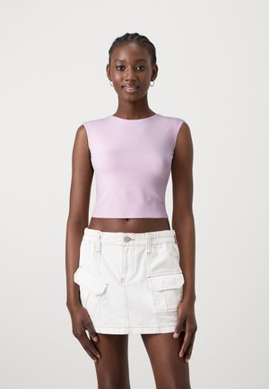 Top corto aderente di un leggero colore viola con una texture liscia, abbinato a una gonna di jeans bianca con tasche frontali e dettagli di cucitura visibili.