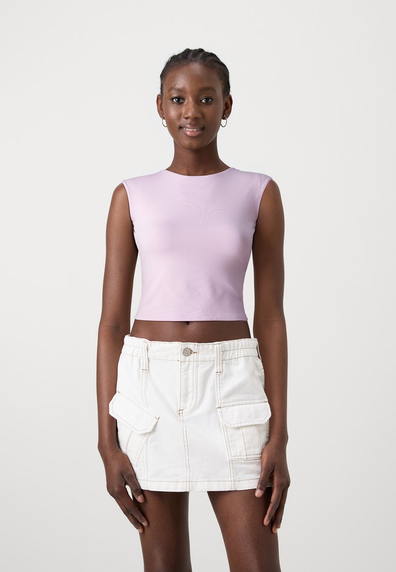 Top corto aderente di un leggero colore viola con una texture liscia, abbinato a una gonna di jeans bianca con tasche frontali e dettagli di cucitura visibili.