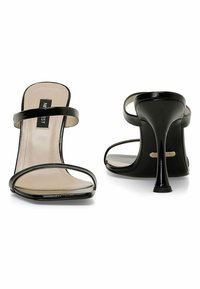 Black high-heeled sandals with two thin straps, open toe design, glossy patent finish, and a tapered heel. Beige insole with logo.