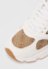 Toe de sneaker-ului din piele albă și țesătură maro cu monogramă, cu șireturi albe și vârf din cauciuc, pe un fundal alb.