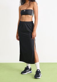 Svart bandeau-top med tre vita ränder, ihopparad med en svart maxikjol med sidsprickor. Bärs med svarta sneakers och vita ankelsockor.