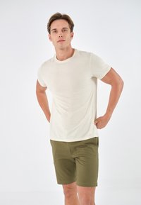 Beige kortermet t-skjorte med rund hals, laget av myk stoff. Kombinert med olivenfargede shorts med skreddersydd snitt og frontlommer.