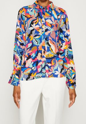 Blouse met knopen en lange mouwen in levendig multicolor abstract bloemenpatroon, gecombineerd met een witte broek, weergegeven van nek tot heupen.