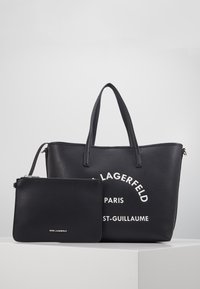 Czarna torba tote Karl Lagerfeld z uchwytami i dopasowaną zipowaną saszetką, wyeksponowana na białej platformie na szarym tle.