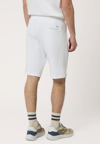 Shorts en coton blancs avec une taille élastique, longueur genou et poche arrière. Assortis à des baskets beiges et marine et des chaussettes rayées.