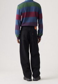 Långärmad skjorta med flerfärgade ränder i grönt, blått och mörkrött. I kombination med lösa svarta jeans och mörka sneakers.