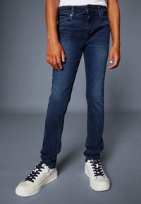 Granatowe obcisłe dżinsy z denimu z pięcioma kieszeniami i subtelnym wyblaknięciem, połączone z białymi trampkami z granatowymi sznurowadłami i bocznym suwakiem.