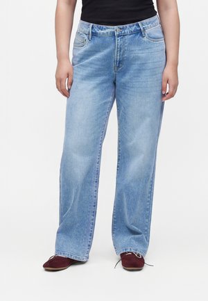 Person wearing light blue wide-leg jeans and dark red flat shoes, standing against a plain light background.