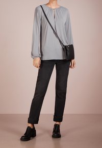 Hellgraue Bluse mit langen Ärmeln und Schlüsselloch-Ausschnitt, kombiniert mit schwarzen Jeans und schwarzen, hohen Ankle Boots; kleine schwarze Umhängetasche.