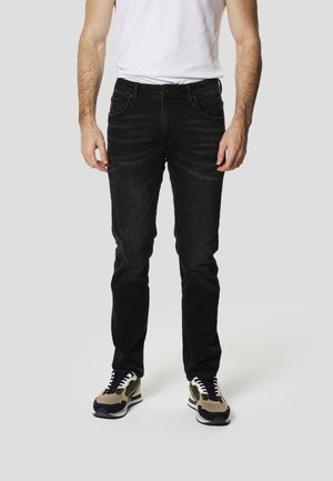 Pantalones vaqueros negros de denim con un diseño de corte ajustado, cinco bolsillos y un sutil desgaste. Combinados con zapatillas beige y negras.