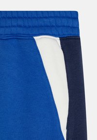 Blå sweatpants har ett texturerat tyg med en vit accentpanel på sidan, kompletterad med en mörk marinblå sektion längst ner.