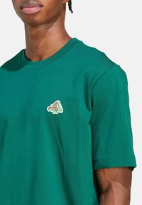 Zelené bavlněné tričko s krátkými rukávy, s malou, barevnou výšivkou pizzy na levé části hrudi.