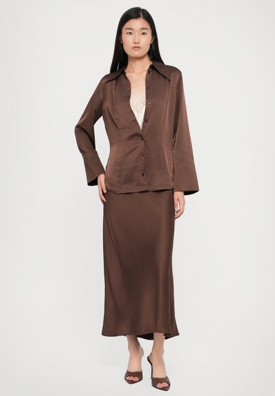 Brown satin long-sleeve shirt with a button front and pointed collar, paired with a matching satin skirt that extends to the ankles.