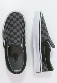 Sneaker slip-on a scacchi neri e grigi con suole in gomma bianca e accenti neri a contrasto, caratterizzati da una tomaia in tessuto testurizzato.