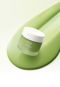 Vihreä TIRTIR Matcha Rauhoittava Voidepurkki valkoisella kannella sileän vihreän voidevaluman päällä taustalla, korostaen rauhoittavaa ihonhoitoa.