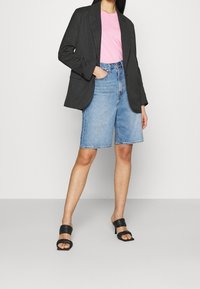 Blazer gris a rayas finas sobre una camiseta de color rosa claro, combinado con pantalones cortos de mezclilla azules y sandalias negras de tacón cuadrado. Estilo casual, corte ajustado.