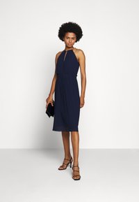 Rochie halter navy cu țesătură plisată, decolteu cu decupaj și talie elastică. Asortată cu tocuri negre cu barete și un clutch negru.