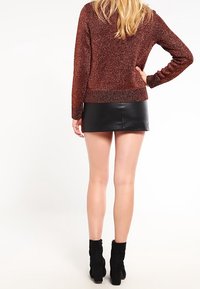 Suéter marrón brillante de punto con un dobladillo acanalado, combinado con una falda mini de cuero negra y botas negras de tobillo. La vista trasera muestra el cabello largo.