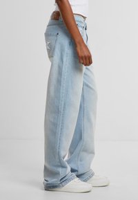 Ljusblå denim byxor med vida ben, synlig sömnad, en läderlapp bak och broderade detaljer på bakfickorna.