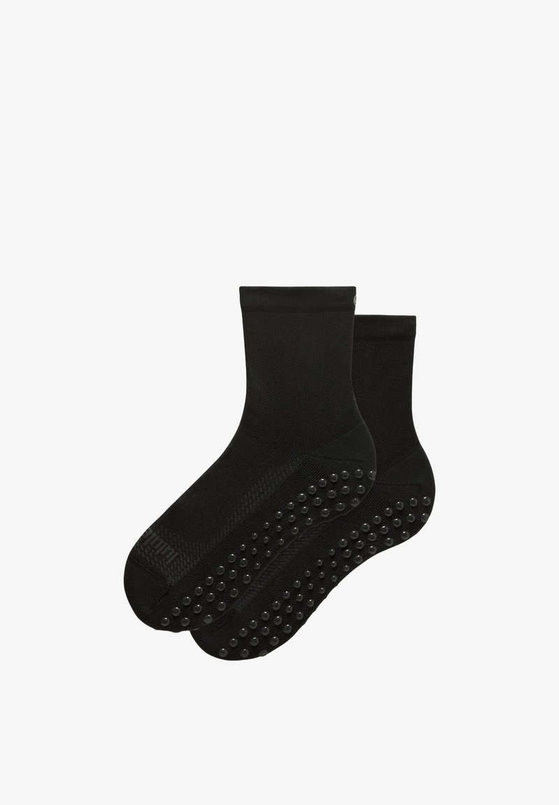 Paire de chaussettes noires pour cheville avec des grips en caoutchouc antidérapants sous la semelle pour une meilleure adhérence et sécurité.