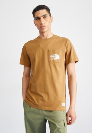 T-shirt in cotone marrone con taschino sul petto decorato con un logo e un testo bianchi. Maniche corte e vestibilità comoda, abbinato a pantaloni cargo verdi.