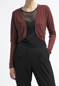 Burgunderfarbener, leichter, langärmeliger Cardigan mit einer kurzen Passform, kombiniert mit einem schwarzen Netzoberteil und hoch taillierten schwarzen Hosen.