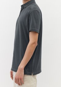 Polo shirt gris foncé en coton respirant, avec un col classique, des manches courtes et un logo discret à l'ourlet. Fentes latérales pour plus de confort.