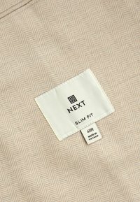 Camică slim fit dintr-un material bej deschis cu un model în zigzag. Eticheta arată marca "NEXT," mărimea 40R și "Fabricat în Vietnam."