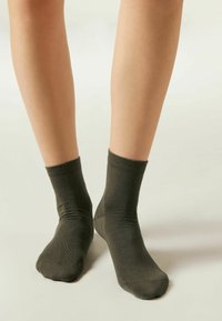 Calcetines tobilleros de color verde oscuro, hechos de un material suave y elástico; textura lisa con un puño acanalado en la parte superior.