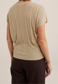 Beige kortärmad stickad topp med vertikal ribbad textur och en figurnära nederdel, kombinerad med mörkbruna byxor.