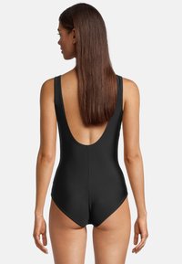Maillot de bain noir avec une conception à dos bas, des bretelles larges et un tissu lisse et élastique pour un look ajusté.