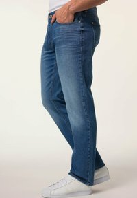 Jeans de mezclilla azul oscuro con corte recto, desvanecimiento sutil y diseño clásico de cinco bolsillos, combinados con zapatillas blancas.