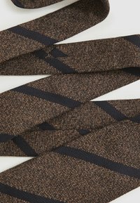 Pruunide ja mustade geomeetriliste mustritega kangast lint, tekstureeritud kude, lai ja lame, tumedama värvi silmapaistvate diagonaalribadega.